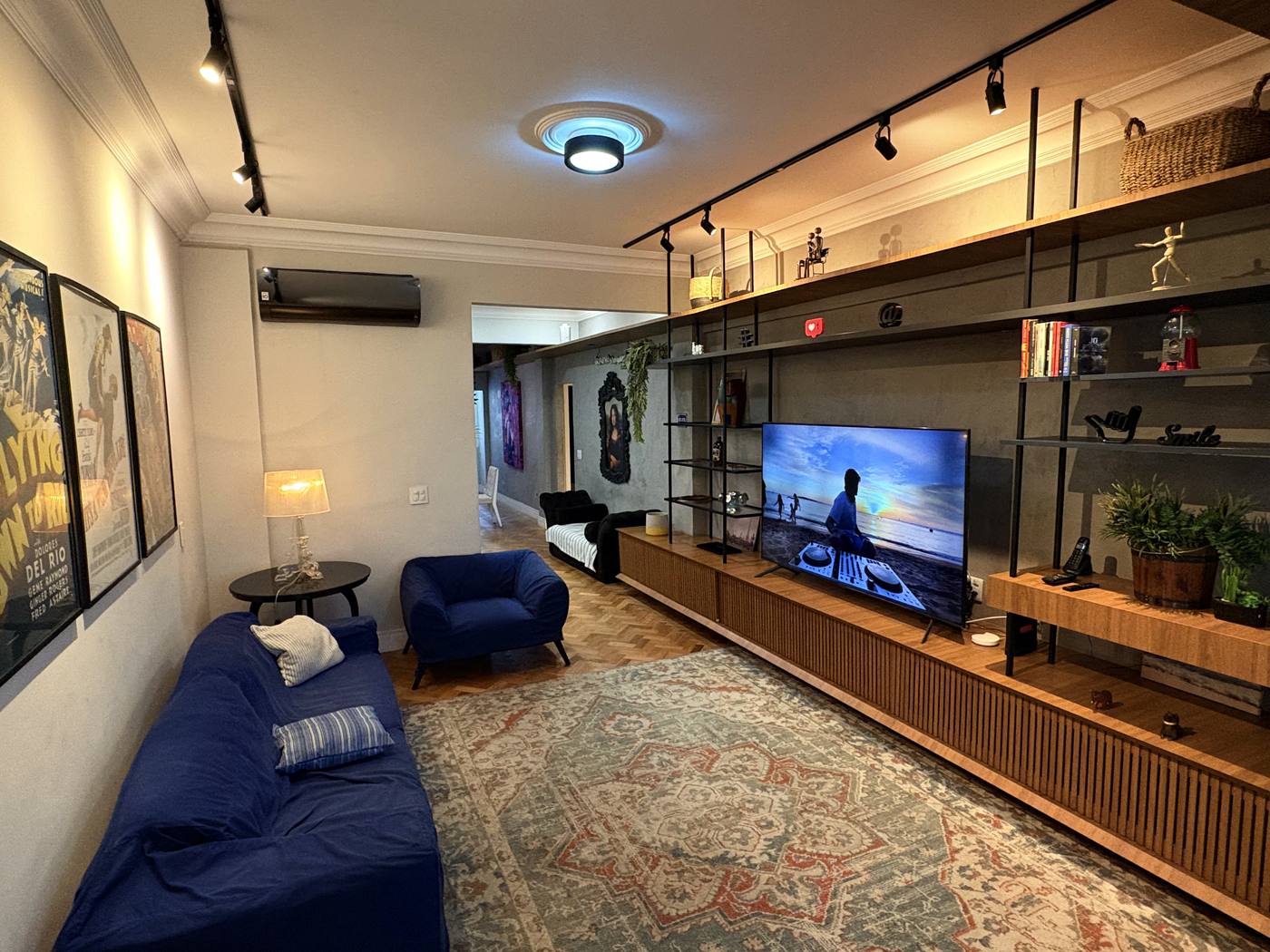 Sala de um apartamento de temporada no Rio, com sofá azul, ar-condicionado na parede, TV e luminária acesa